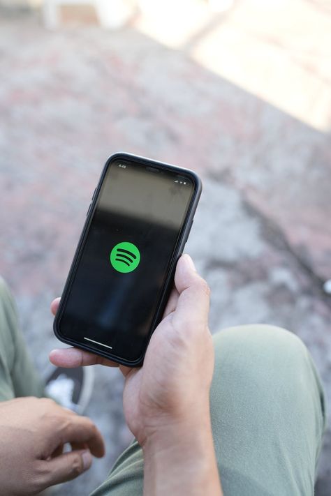 A person holding a cell phone with the spotify app on it · Free Stock Photo Person Holding Phone, Music Streaming App, Holding Phone, Radio Channels, Blur Photo, Spotify App, On Phone, Iphone Photos, The Cell