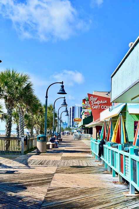 View of the Myrtle Beach Boardwalk and Promenade with palm trees lining the boardwalk and various shops, including the Gay Dolphin Gift Cove, under a clear blue sky. Myrtle Beach Boardwalk, Trivia Time, Beach Boardwalk, You Get It, Myrtle Beach, Trivia, Get It