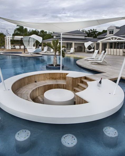 A small walkway continues from the wood pool deck to wood stairs descending into a pool level bar. The bar features white countertop and a white island in the center surrounded by a wood bench. Stone stools are built in underwater surrounding the bar feature for fun swim-up seating. A triangle canvas cover offers shade to the bartender for the perfect entertaining atmosphere. Pool Bar Design, Wood Pool Deck, Caribbean Villas, Outdoor Kitchen Bars, Storage Inspiration, Swim Up Bar, Luxury Pools, Belek, Pool Bar