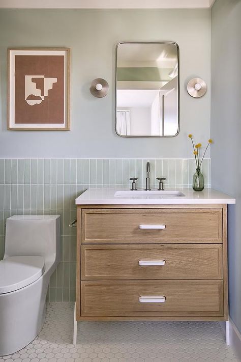 Green vertical stacked tiles complement a pale green bathroom wall holding a curved nickel mirror over a brown dresser-like washstand finished with white pulls and dark nickel gooseneck faucet. Pale Green Bathroom, Stacked Subway Tile Bathroom, Nickel Mirror, Bathtub Cover, His And Hers Sinks, Brown Dresser, Beach House Bathroom, Subway Tiles Bathroom, Shower Wall Tile