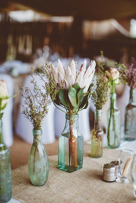 rustic wedding centerpieces flowers in blue glass bottles of different shapes on a linen tablecloth kikitography Protea Bouquet, Tafel Decor, Recycled Glass Bottles, Cactus Succulents, Eco Wedding, Unique Wedding Flowers, Wedding Floral Centerpieces, Rustic Wedding Centerpieces, Eco Friendly Wedding