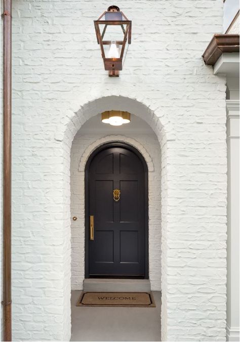 A white painted brick Tudor house with arched doorways, black front door, and copper downspouts. White Painted Brick Exterior, The Fox Group, Fox Group, Arched Front Door, Painted Brick Exteriors, Timeless Interior Design, Painted Brick House, Brick Arch, Black Front Doors