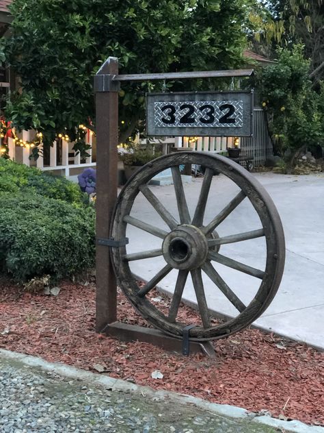 Wagon Wheel Address Sign Ideas, Wagon Wheel Garden Decor, Landscaping With Wagon Wheels, Farmhouse Wagon Wheel Decor, Wagon Wheel In Garden, Wagon Wheel Address Sign, Wagon Wheel Yard Decor, Rustic Wagon Wheel Decor, Diy Wagon Wheel Decor