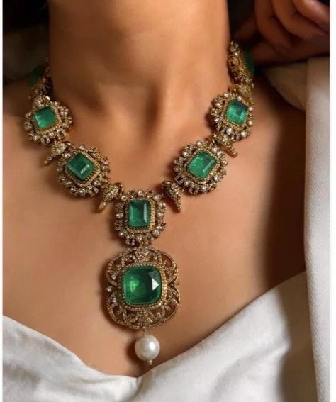 This exquisite Victorian doublets statement necklace set in emerald green captures the essence of opulence and vintage charm. The necklace, crafted with meticulous detail, features gleaming emerald green doublets set in an ornate Victorian-style framework. Each doublet, with its rich hue and intricate facets, reflects light beautifully, creating a mesmerizing play of colors.  The necklace cascades gracefully, adorned with smaller emerald accents and delicate filigree patterns that evoke the gran Emerald Jewelry Necklace, Victorian Jewelry Necklace, Filigree Jewellery, Emerald Necklaces, Simple Cocktail Dress, Sabyasachi Jewelry, Emerald Jewellery, Victorian Style Jewelry, Long Necklace Set