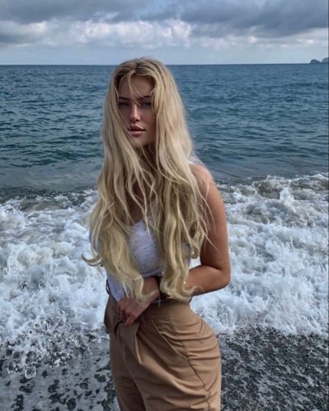 Portait of a girl at the beach. She has long blond hair which is quite wavy because of the salty water. It’s the definition of beachy waves. Eyes looking straight at the camera. The picture gives off dreamy vibes