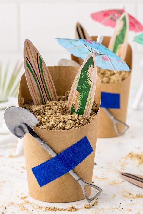 A beach themed sand pudding dessert with surf boards and paper umbrella. Sand Bucket Dessert, Sand Pudding Cups, Sand Pudding Dessert, Surf Board Cake, Totally Twobular, Sand Pudding, Pudding Cup Recipes, Surf Birthday Party, Themed Birthday Party Ideas