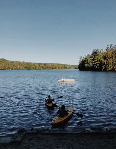 Photo of two kayakers paddling away from a beach on a pond with blue water, a dock, and green trees on the horizon New Hampshire Summer, East Coast, New Hampshire, Kayaking, New England, Natural Landmarks, Water, Travel