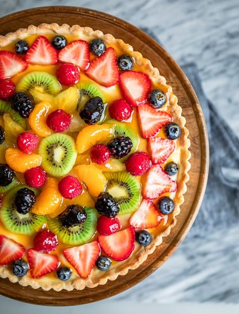 An overhead shot of fresh fruit tart on a wooden stand. Fruit Tart Breakfast, Classic Fruit Tart, La Madeleine Fruit Tart Recipe, Homemade Fruit Tart, Fruit Torte Cake, Best Fruit Tart Recipe, Whole Foods Fruit Tart Recipe, Fruit Tart Pie, Fresh Fruit Tart Recipe