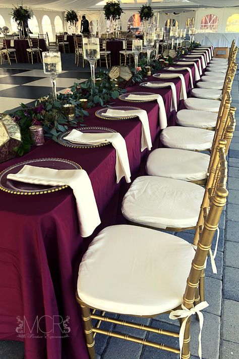 An elegant art deco themed wedding with burgundy linens and gold accents. An abundance of greenery lines the long head table, floating candles in wine glass vases and gold geometric lanters add both vintage and modern elements to the wedding decorations. Gold chiavari chairs with ivory cushions and napkins brighten the decor and match the black and white checkered dance floor. #dream #dreamwedding #centerpieces #reception #weddingreception #dancefloor #october #octobercolors Chivari Chairs Wedding, Long Head Table, Art Deco Themed Wedding, Wedding Decorations Gold, Head Table Design, Checkered Dance Floor, Gold Chivari Chairs, Art Deco Wedding Theme, Gold Chiavari Chairs