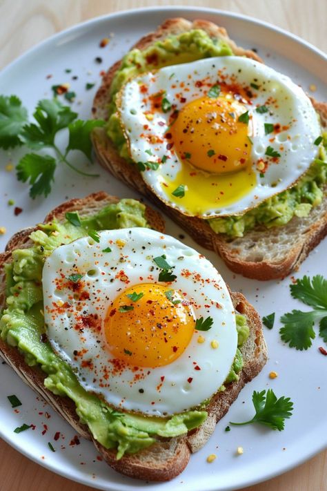 Two slices of avocado toast topped with fried eggs and a sprinkle of red seasoning, garnished with fresh cilantro leaves on a white plate. Breakfasts With Avocado, Healthy Vegetarian Recipes Breakfast, Breakfast Ideas Avocado Toast, Toppings For Toast, Easy Breakfast Toast Ideas, Easy Breakfast Toast, Healthy Breakfast Avocado Toast, Healthy Recipes Breakfast Easy Mornings, Romanticize Your Morning