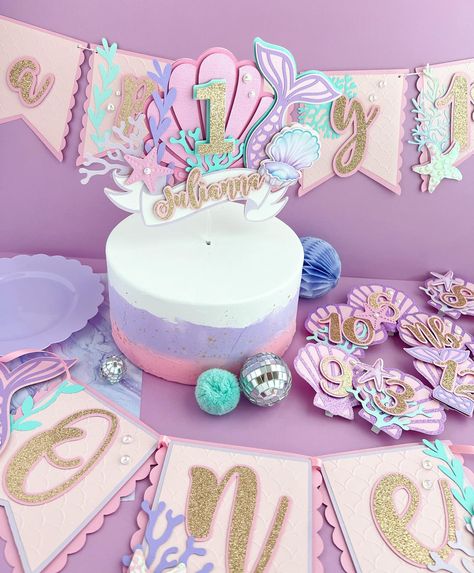 A super cute Mermaid theme decor for a little ones first birthday 🧜🏻‍♀️🫧 Using tones of pink, purple and turquoise, and iridescent….this order came out so cute! What do you think? This first birthday party package included Cake topper High chair banner Milestone cards Happy Birthday banner Name banner & Centerpieces . . . #mermaidcenterpieces #mermaidparty #milestonephotography #milestonebanner #mermaidpartydecorations #mermaidpartyideas #undertheseaparty #papeleriapersonalizada ... Mermaid Theme Smash Cake, Mermaid High Chair Banner, Mermaid Number Decor, Pink And Blue Mermaid Cake, Under The Sea Birthday Banner, Cards Happy Birthday, Baby First Birthday Themes, 1st Birthday Cake Topper, Mermaid Party Decorations