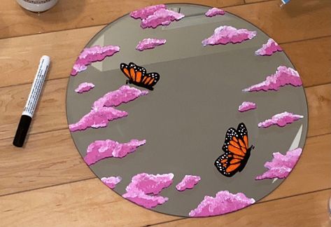 This is a round mirror with a beautiful painting of pink clouds and orange butterflies. It is 35.56cm x 35.56cm x 0.38cm. It is made with acrylic paint and can be cleaned with Windex! Order yours today. [DOES NOT COME WITH HANGING PIECE ON BACK] Cloud Painting On Mirror, Round Mirror Painting, Diy Mirror Painting Ideas, Mirror Frame Painting Ideas, Diy Round Mirror, Mirror Painting Ideas, Spiegel Diy, Orange Butterflies, Painting Glass Jars