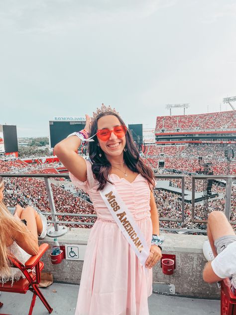 Stadium background single individual wearing a short pink dress with puffed sleeves pink heart shaped glasses a white sash with gold writing that says “miss Americana” and a gold and pink tiara on her head Miss Americana And The Heartbreak Prince Eras Tour Outfit, Ms Americana And The Heartbreak Prince Taylor Swift Costume, Miss Americana Costume Eras Tour, Heartbreak Prince Outfit Taylor Swift, Miss Americana Costume Taylor Swift, Miss Americana And The Heartbreak Prince Taylor Swift Costume, Miss Americana Outfit Eras Tour, Ms Americana Taylor Swift Costume, Miss Americana And The Heartbreak Prince Outfit