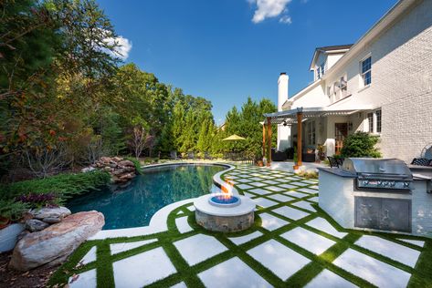 Freeform pool with outdoor kitchen, firepit, tanning ledge, pergola, and limestone paver deck in offset with turf ground inlay. #freeformpools Small Backyard With Pool And Turf, Freeform Pool Landscaping Ideas, Pool With Pavers And Turf, Turf And Tile Patio, Turf And Paver Pool Deck, Pool Landscaping Pavers, Pools With Turf Decking, Travertine And Turf Pool Deck, Pool Turf Ideas