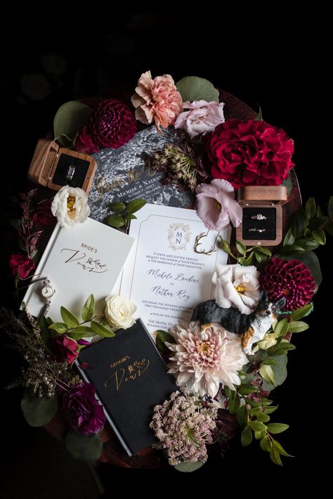 The image presents an elegant wedding arrangement, featuring a mix of vibrant and soft-hued flowers, a ring box, and intricately designed wedding notebooks. A delicate timepiece, a miniature dog figurine, and jewelry are artfully placed within the floral assortment, all resting on a dark surface that enhances the rich colors and textures of the composition. This tableau exudes a romantic and personalized vibe, suggesting a celebration of love and meticulous planning. Wedding Flatlay, Unique Wedding Invitation, Miniature Dog, Wedding Invitation Inspiration, Dark Wedding, Moody Wedding, Editorial Wedding, Fall Weddings, Invitation Inspiration