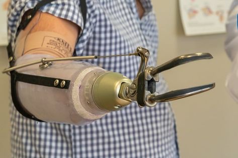 A close up on a body powered prosthetic arm with a hook. The prosthetic is pale brown with black parts, the hook is metallic and the person is wearing a blue and white plaid shirt with short sleeves. Arm Prosthetic, Prosthetic Arm, Autumn Design, Strong Hand, Drawing Cartoon Characters, Sand Bag, Heavy Bags, Drawing Cartoon, Fall Design