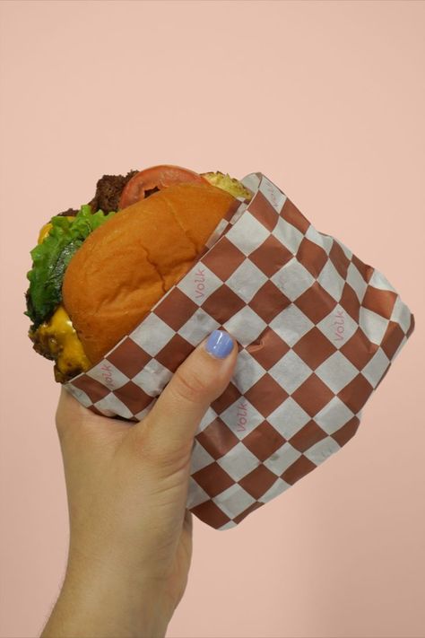 Hand with blue nails holds up shake shack burger against a peach background. The burger is wrapped partially in a terracotta and white check pattern. In the white cells, Volk is typed in soft pink color. Burger has lettuce, tomato, cheese, and pickles peeking out the side. Burger Wrap, Burger Packaging, Sandwich Packaging, Clever Packaging, Sandwich Wrap, Wrapping Paper Design, Letterpress Invitations, Print Studio, Food Packaging Design