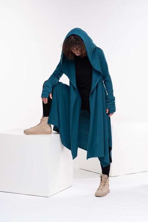 Wool Cape, Knit Cardigan, Cloak with HoodThis asymmetrical and modern cloak with hood has two side pockets, super comfy hood and thumb holes for a fabulous look.The model in the picture is 176cm. ⅼ 5.8 ft. tall and is wearing size S / color: Teal🌟 INFO:• Worldwide EXPRESS shipping – please provide a phone number for shipping documents• US Sizing XS to 4XL – body size chart available below• We offer customization to Personal Measurements & Larger Sizes 5XL, 6XL, 7XL ….🌟 MATERIAL & CARE• Hoodie Around Waist, Cloak With Hood, Long Knitted Cardigan, Shipping Documents, Winter Cloak, Futuristic Clothing, Cardigan Hoodie, Cape Cloak, Cape Sweater