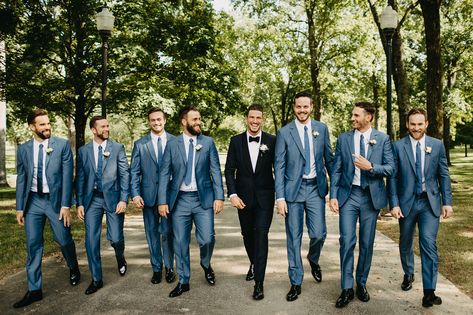 Groom in Classic Black Tuxedo with White Boutonniere | Groomsmen in Matching Blue Suits with Blue Ties | Menswear Wedding Attire Blue Suit Groom Black Suit Groomsmen, Grooms Color Suits, Navy And Black Suit Wedding, Blue Groom Black Groomsmen, Dark Blue Tuxedo Wedding Groomsmen, Black Tux Groom Blue Suit Groomsmen, Groom Black Suit Groomsmen Navy, Blue And Black Groomsmen Attire, Black Suit Light Blue Tie Wedding