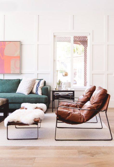 Eclectic modern living room area, green couch pushed against wall with white wainscoting detail. The right of the couch are two brown, modern leather chairs with matching ottomans. Thrown over the ottomans are faux sheepskin throws. Modern Ottomans, Poltrona Design, Wainscoting Wall, Leather Ottomans, Wall Detail, Sofa Green, White Wainscoting, Deco Led, Sofa Leather