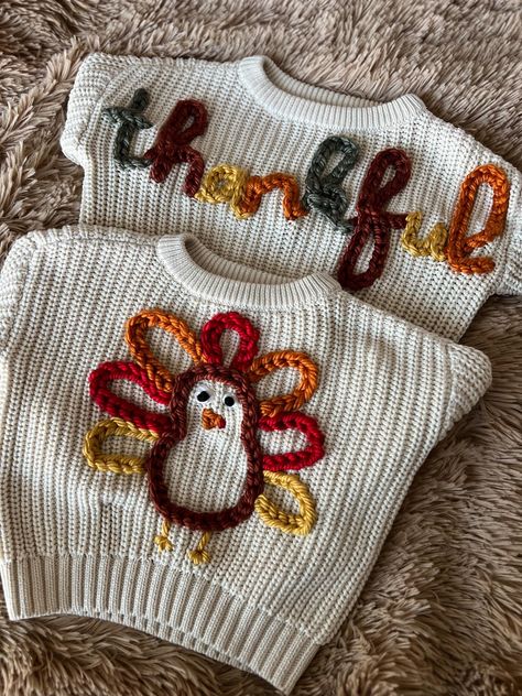 HAND-EMBROIDERED SWEATER -- This listing is for you choice of one hand-embroidered Thanksgiving sweater. This cream sweater features either a multi-colored turkey or the word "thankful" in alternating fall yarn colors. These chunky knit kids' sweaters are made with soft, breathable cotton, are great for daily wear, and look fantastic over jeans or leggings! These sweaters have a round neck and long sleeves, and are made to fit a bit oversized. Recommended care: Hand wash or wash on gentle cycle Thanksgiving Embroidery Designs For Kids, Pumpkin Embroidery Sweater, Yarn Embroidered Sweater, Embroidery Sweater Ideas, Embroidered Knit Sweater, Embroidered Name Sweater, Sweater Embroidery Diy, Thanksgiving Embroidery, Sweater Embroidery