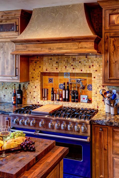 Rustic wood kitchen cabinets with beautiful wood grain are paired with dark brown countertops and earth-toned tiled backsplash in this Mediterranean kitchen. A pro-quality bright blue oven adds a burst of color to the space. Rustic Wood Kitchen Cabinets, Brown Countertops, Blue Oven, Mexican Style Kitchens, Mediterranean Kitchen Design, Spanish Style Kitchen, Rustic Kitchen Cabinets, Mediterranean Kitchen, Mexican Kitchens