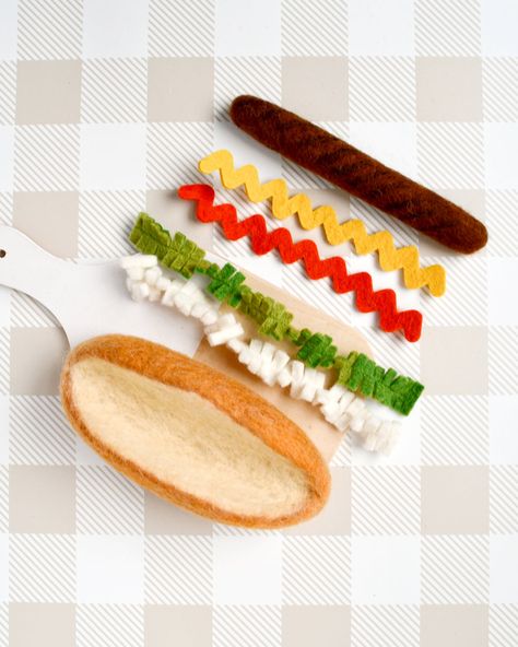 Felt Hot Dog Set - deconstructed for endless pretend play. Unleash your child's creativity with our Felt Hot Dog Set, designed for interactive and imaginative play. This set includes: A soft felt bread roll A felt sausage A strip of white chopped onions A strip of green pickle relish A strip of tomato sauce A strip of mustard With these colourful and detailed pieces, your little one can make a hot dog just the way they want. Whether they prefer a classic combination or an adventurous new creation, this set encourages hands-on fun and culinary imagination. Perfectly sized for small hands, our Felt Hot Dog Set is a delightful addition to any child's pretend food collection, play kitchen, picnic setup, or play shop. Each item is meticulously needle-felted using dense wool dyed with non-toxic Felt Food For Play Kitchen, Felt Food Free Patterns, Felt Food Toys, Diy Felt Food Patterns Free, Felt Food Ideas, Felt Food Patterns Free Templates, Felt Sausage, Felt Pickle, Felt Hot Dog