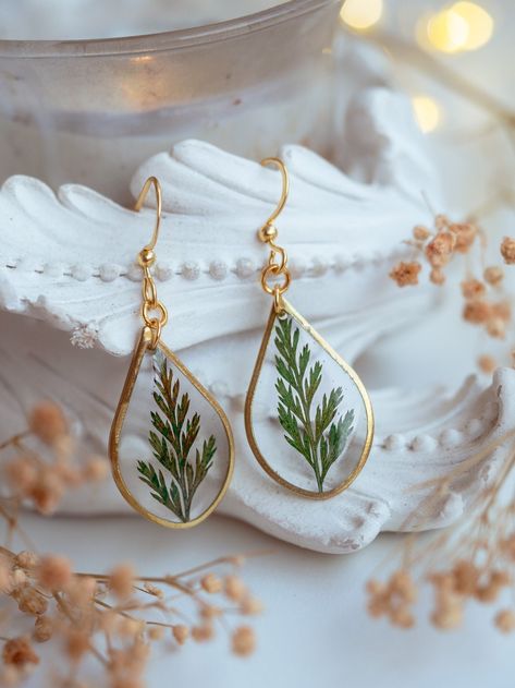 Step into a world of natural charm with our enchanting Fern Leaf Earrings. Crafted with delicate precision, these earrings feature real dried fern leaves, encased in a crystal-clear resin teardrop. Encircled by a finely detailed gold metal frame, each earring resembles a mystic artifact of nature, bringing a touch of the outdoors to your style. These earrings showcase an understated elegance, making them a light, beautiful, and romantic accessory for any occasion. Whether you're buying for yours Cheap Natural Earrings As Gift, Dried Fern, Fern Earrings, Pressed Fern, Resin Light, Brass Frames, Artsy Jewelry, Earring Inspo, Plant Earrings