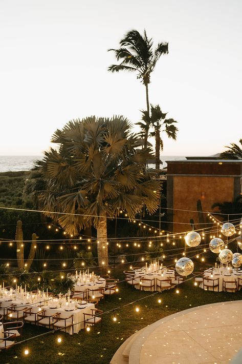 A tropical wedding setup by the beach featuring hanging disco balls and string lights for a fun and glamorous touch. Perfect for couples looking to blend elegance with a bit of party energy in a Baja or coastal-inspired wedding setting. #DiscoBallWedding #OutdoorWedding #BeachReception #TropicalWeddingInspo #BajaWedding Jungle Disco Wedding, Tropical Landscape Lighting, Tropical Outdoor Wedding, Hanging Disco Balls, Cocktail Hour Wedding Decorations, Beach Wedding Aesthetic, Disco Ball Wedding, Wedding Table Details, Tropical Outdoor