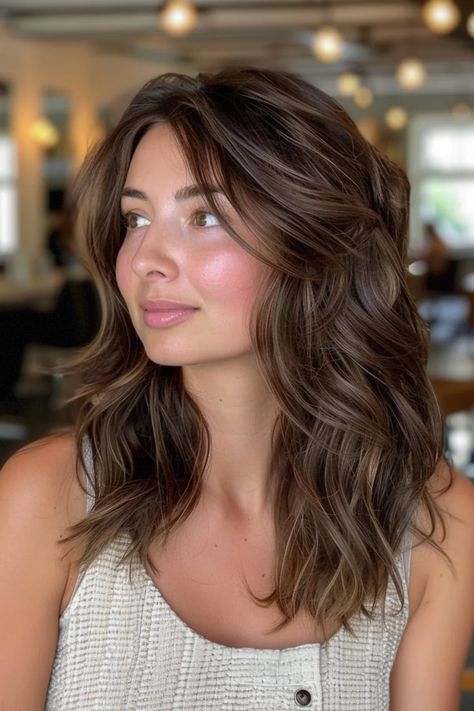 Woman with wavy brown hair gazing to the side, in a softly lit room. Hair Color For Bronze Skin, Chocolate Lowlights, Warm Brunette Balayage, Cherry Highlights, Bronze Balayage, Cinnamon Brown Hair Color, Red Brunette Hair, Cinnamon Brown Hair, Chocolate Brown Hair Color Ideas