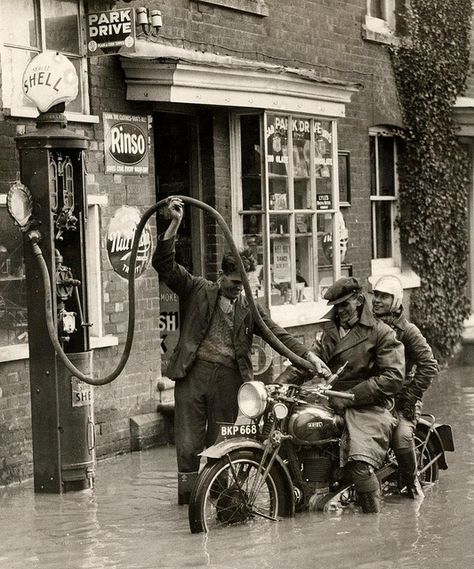 Shell. England 1935. A gas station attendant fills the tank on a motorcycle carrying two people during a small flood. Everyone seems so chipper. Gas Station Attendant, Shell Gas Station, Old Gas Pumps, Vintage Foto's, Motos Vintage, Vintage Gas Pumps, Pompe A Essence, Station Service, Old Gas Stations