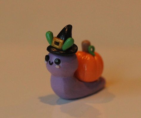 Handmade clay snail with pumpkin on its back. Snail is a light purple color and has  a witch hat on. All pieces are handmade and my differ slightly from the picture. Clay Date Ideas Halloween, Snail Pinch Pot, Air Dry Clay Snail, Polymer Clay Snails, Halloween Clay Figures, Polymer Clay Halloween Ideas, Air Dry Clay Halloween Ideas, Snail Pumpkin, Fall Clay Ideas