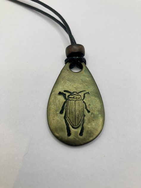 This is a 1 1/2 inch x 1  inch lightweight Beetle Pendant made with Black Premo polymer clay. Stamped by hand using mica powder to shine. It has 16 inch black cord, lobster claw clasp, and decorative bead.  Beads will vary in color from bead pictured in product photo. This necklace is fully hand made and hand finished so slight variations in color/finish should be expected. Mica Powder color will shine differently in different light. Metal Necklace Handmade, Clay Necklace Pendant Aesthetic, Clay Lobster, Beetle Pendant, Bohemian Clay Jewelry, Beetle Necklace, Bug Necklace, Clay Beetle, Clay Pendant Necklace