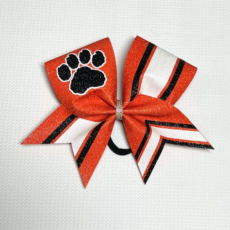 Custom Paw Print Cheer Bow Your choice of base glitter color (shown in orange) Your choice of two accent glitter colors (shown in black and white) 3 paw styles to choose from  All bonded to  coordinating 3in grosgrain ribbon Coordinating Rhinestone Center or Glitter Center Attached to a black hair tie PLEASE NOTE: I may contact you after your order is placed to confirm details, if needed.  CUSTOMIZATION BOX:  Please leave Main color, accent colors and mascot name. DROP DOWN MENU: Choose the paw style you'd like. Choose rhinestone or glitter center. (Glitter center will be main glitter color) Contact me if you have any questions. Visit us on Instagram for more photos of this bow! All bows come carefully packaged in a box to maintain the bows shape. Cheer Apparel, Black Hair Tie, Sideline Cheer, Team Cheer, Custom Cheer Bows, Spirit Gear, School Cheer, High School Cheer, Cheer Ideas