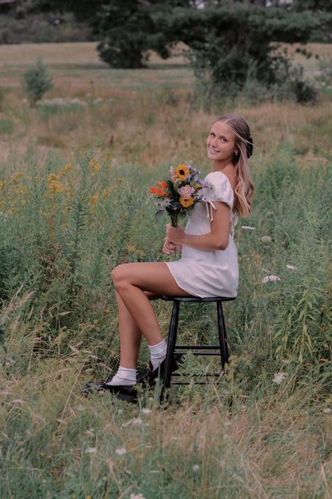 Senior photo with chair and flowers Chair Poses Senior Pictures, Senior Pictures In Chair, Senior Photos Chair In Field, Senior Picture Ideas Chair, Senior Picture Ideas Stool, Stool Senior Pictures, Senior Picture Ideas Holding Flowers, Stool Photoshoot Photo Ideas Outside, Senior Pictures With Stool