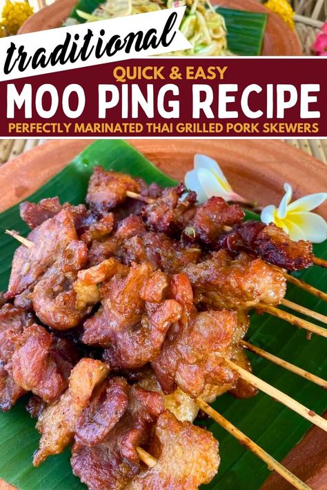 Several moo ping (Thai grilled pork skewers) on a banana leaf in a clay dish with 2 flowers in it as well.