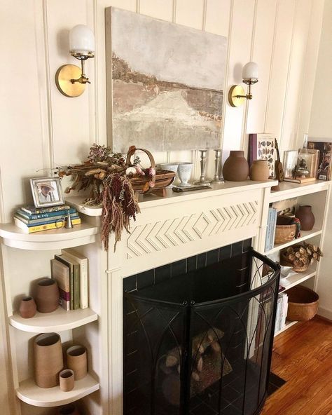 Neutral living room with a traditional fireplace and boho accessories like books, brown vases, and dried flowers Room Improvement, Neutral Interior Design, Travel Inspired Decor, Cottage Lighting, Sconces Living Room, Black Interior Design, Wall Lights Living Room, Library Shelves, Sazerac