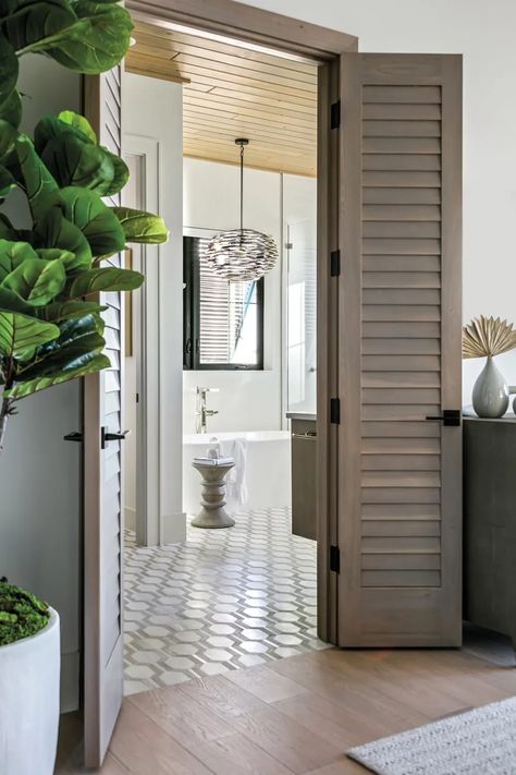 Introducing a West Indies vibe, custom louvered doors in the main bedroom open to the suite’s bathroom, marked by Jeffrey Court’s Montgomery Mosaic flooring and a stained tongue-and-groove white oak ceiling. An RH stool and an Arteriors pendant accent the Victoria + Albert tub and Brizo filler from Ferguson Bath, Kitchen & Lighting Gallery. West Indies Bathroom, White Oak Ceiling, West Indies Interior, British Colonial Bedroom, West Indies Home, Oak Ceiling, British West Indies Style, Louvered Doors, West Indies Style