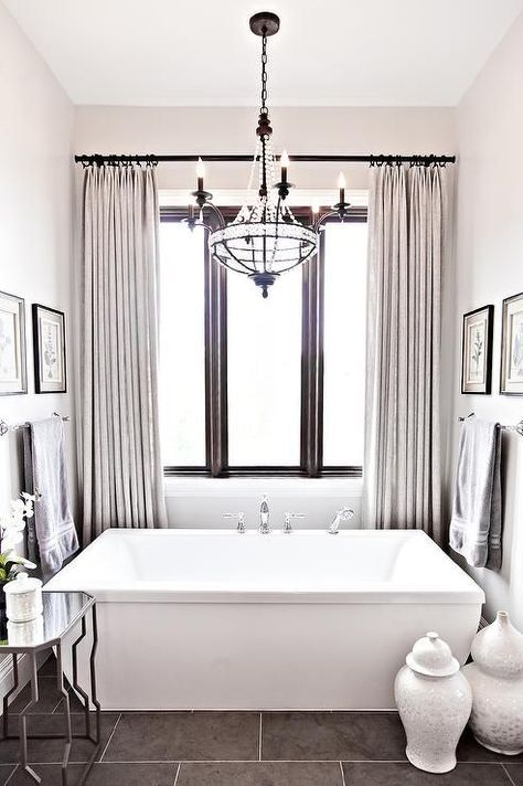 Sophisticated bathroom features a clear beaded Paris flea market chandelier hanging over a freestanding rectangular bathtub fitted with a decl mount tub filler placed under a window dressed in light gray French pleat curtains. Bathroom Lighting Over Tub, Tub Chandelier, Bathroom Window Curtains, Hgtv Star, Sophisticated Bathroom, Bathtub Design, Bathroom Tub, Freestanding Bath, Bathroom Windows