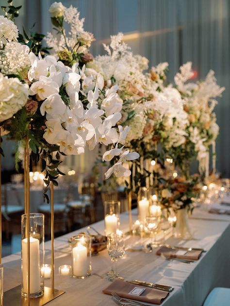 Elevated long table centerpiece floral arrangement with candles on open gold stands. Wedding head table flowers. Elegant Long Table Centerpieces, Gold Rectangle Wedding Centerpiece, Elevated Centerpieces Wedding, Tall Flower Centerpieces With Candles, Long And Low Floral Centerpiece, White Floral Runner Centerpiece, Elevated Floral Centerpieces White, Head Table Flowers, Long Table Centerpieces