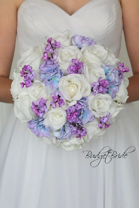 This is a round brides bouquet with white roses with jewel centers accented with purple/capri blue hydrangea and small purple lilacs. All of our wedding bouquets are made with artificial wedding flowers. Bouquet With Lilacs, White And Lavender Wedding, White Brides Bouquet, Blue Purple Wedding, Davids Bridal Gowns, Lilac Wedding Bouquet, Blush Bouquet Wedding, Purple Wedding Bouquets, Purple Wedding Theme