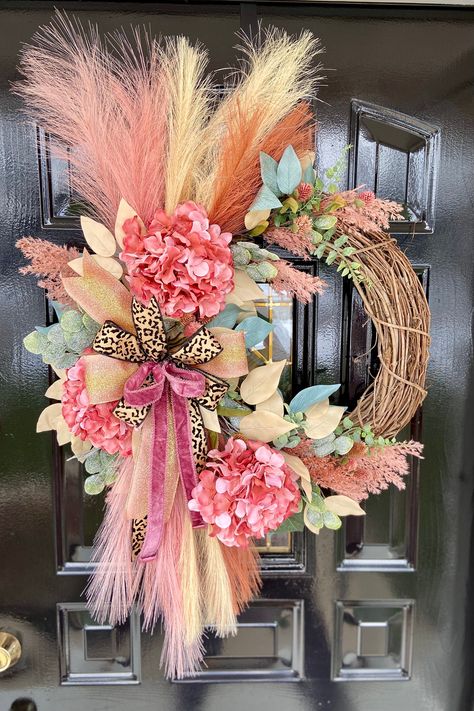 This wreath features a natural twig base adorned with an array of artificial decorative elements. A stunning mix of pink hydrangeas and delicate foliage are tastefully arranged to create a full, lush look. Eye-catching pampas grass in shades of pink, rust and blonde add height and texture, while beige and green leaves give a hint of sparkle. The centerpiece is a chic leopard print bow tied with a combination of velvet and glitter ribbons in rose and gold, with long tassel ends that gracefully dr Faux Floral Wreath, Pink Fall Wreaths For Front Door, Boho Wreaths, Pink Fall Wreath, Butterfly Wreath, Pampas Wreath, Spring Wreath Ideas, Floral Door Wreaths, Boho Wreath