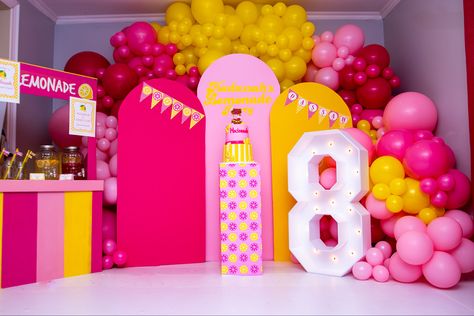 Pink, Fuchsia and yellow balloons used for a pink lemonade party. Pink, fuchsia and yellow backdrop with “Hadassah’s lemonade party” written on it. A lemonade stand is on the left side of the picture with some lemonade and pink lemonade on it. Lit up Marquee letter 8 display in front of backdrop and cake stand with a pink lemonade cake on it Lemonade Party Decorations, Yellow Party Decorations, Pink Lemonade Party, 18th Bday, Yellow Party, Lemonade Party, Yellow Balloons, Green Balloon, Barbie Party