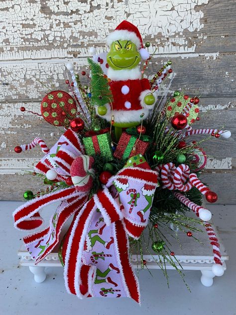 Christmas Centerpiece Christmas table centerpiece Christmas floral arrangement table decor Santa Elf This Christmas arrangement will look great as a centerpiece for your table or anywhere you want to add Christmas cheer. The arrangement is on a metal white tray with greenery, sprays, ball picks, candy picks, adorable Santa holding a tree with garland of lights and a holiday bow.  Measures approx. 16"H X 12"W SHIPPING FEE IS INCLUDED IN LISTING PRICE  Please check out my other listings and Thank you for looking! Please follow me on Pinterest" for all of my latest and past designs  Link: https://www.pinterest.com/cylesdazzlingdesigns/boards/ Please follow me on Facebook "CylesDazzlingDesigns" for all of my latest designs and/or Custom order your design. Link: https://www.facebook.com/cylesda Grinch Arrangement, Grinch Centerpiece, Tree With Garland, Grinch Diy, Centerpiece Christmas Table, Candlestick Arrangements, Music Centerpieces, Table Centerpiece Christmas, Christmas Tree Village Display