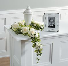 White rose flowers, urn, and matching photo frame memorial. Just one of 14 Funeral Urn Memorial Service Table Arrangement Ideas Cremation Urn Display, Urn Arrangements, Flower Urn, Casket Sprays, Memory Table, Diy Arrangements, Memorial Flowers, Sympathy Flowers, Floral Garland