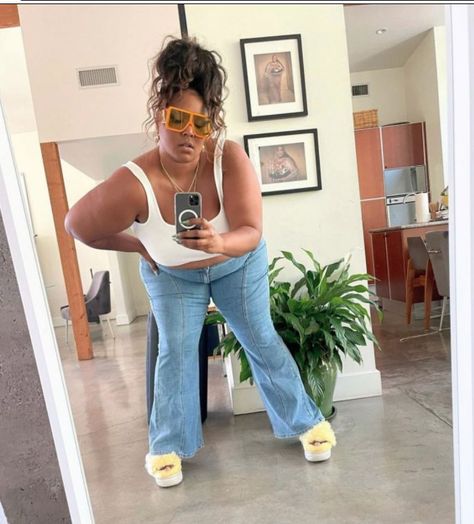 Lizzo taking a selfie wearing a white tank top, light wash wide leg jeans with a center seam, fuzzy yellow platform sandals, oversized orange aviators, and a messy top knot Lizzo Outfits Casual, Lizzo Wallpapers, Lizzo Aesthetics, Annika Osterlund, Lizzo Outfit, Lizzo Outfits, Lizzo Concert, Celebrity Face Claims, Fame Shifting