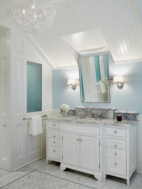 Under a white beadboard sloped ceiling illuminated by a Serena & Lily Flora Chandelier, a polished nickel rectangular pivot mirror is flanked by nickel and glass sconces mounted on a pale blue wall above a white breakfront washstand completed with polished nickel knobs and a gray marble countertop and a rectangular under mount sink located beneath a nickel faucet fixed to a gray marble backsplash. Bathroom Sink Under Sloped Ceiling, Sloped Ceiling Bathrooms, Beadboard Sloped Ceiling, Angled Ceiling Bathroom Vanity, Beadboard Bathroom Ceiling, Sloped Bathroom, Mirror Over Sink, Sloped Ceiling Bathroom, Beadboard Trim