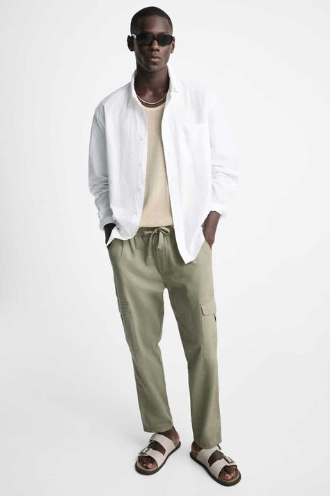 Men's green cargo pants, knit cream T-shirt, open white shirt and stone sandals outfit. This outfit was included in the article: What Colours To Wear With Green Pants: 7 Foolproof Shirt Options, on MensFlair.com Light Green Pants Outfit Men, Olive Green Pants Men, Green Khaki Pants, Green Pants Men, Green Chino Pants, Colored Pants Outfits, Green Pants Outfit, Shirt Outfit Men, Olive Green Pants