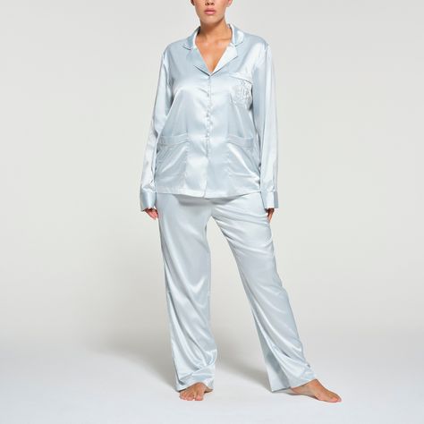 Get your best rest in this sophisticated-chic sleep set. Made with our luxe, silky fabric, this two-piece set features a button-up long sleeve with tonal SKIMS embroidery at the chest pocket and a relaxed, straight-leg pant with an adjustable drawstring at the waist. Comes specially packaged in a branded gift box. Fits true to size. | SKIMS Long Sleeve Button Up Pajama Set | Blue | Medium | SKIMS Hotel Shine Skims Pajamas, Embroidered Pajamas, Silk Pjs, Button Up Pajamas, Silky Fabric, Sleep Set, Christmas Wishlist, Straight Leg Pants, Chest Pocket