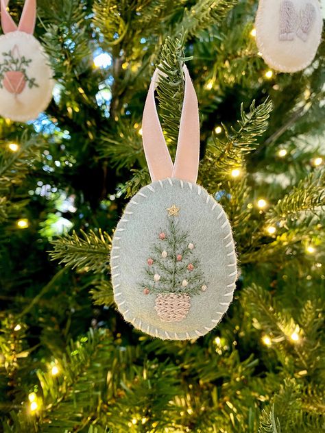 "This one-of-a-kind handmade and embroidered ornament features a decorated Christmas tree in a woven basket. It is embroidered with tiny stitches onto 100% Merino wool felt in a light sage green color and is lightly filled with polyester fiber filling. The ornament hangs from a pale pink velvet ribbon. This ornament is soft. Perfect for families with children or pets. *Hand-embroidered *100% Merino wool felt *Velvet ribbon *Polyester filling *Measures: Height: 2.5\" (4.5\" including ribbon); Wid Twelve Days Of Christmas Felt Ornaments, Heirloom Christmas Tree, Felt And Embroidery Projects, Felt Ornaments Embroidered, Felt Applique Ornaments, Hand Stitched Christmas Ornaments, Pink Felt Christmas Ornaments, Christmas Decorations Embroidery, Pink Felt Ornaments